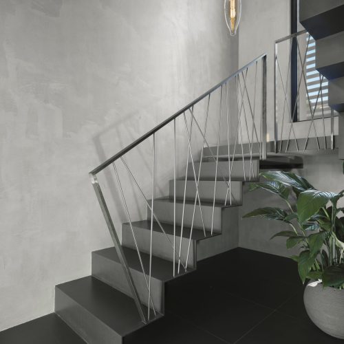 modern staircase with designer handrail, on the right there is a houseplant the stairwell is illuminated of a modern suspended lamp