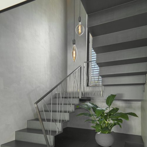 modern staircase with designer handrail, on the right there is a houseplant the stairwell is illuminated of a two modern suspended lamps